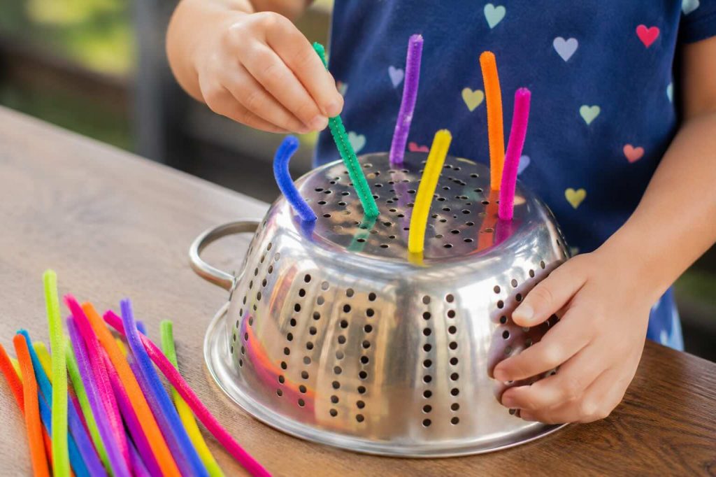 kid playin with pipe cleaners and a colander