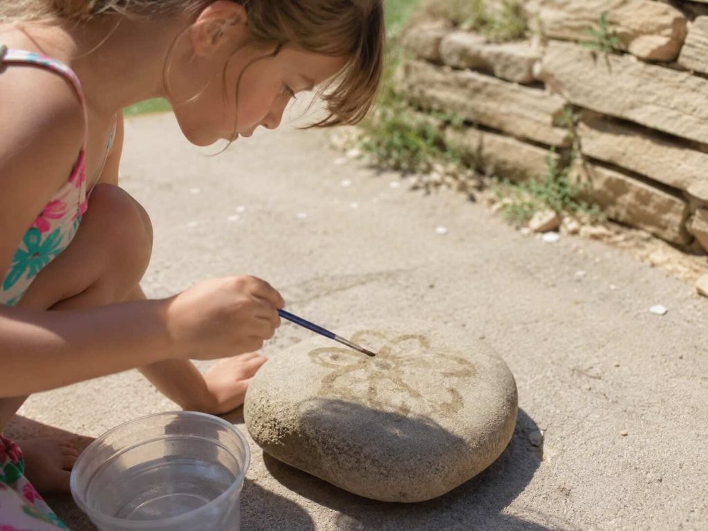 child painting water on a rock outside