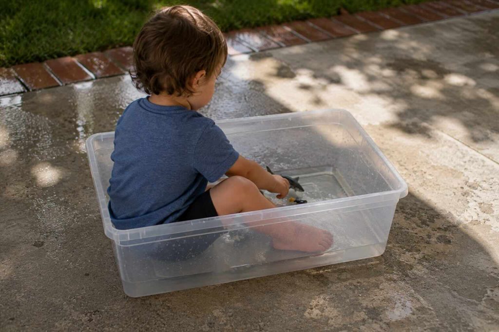 child sitting in a small container of water playing with toys